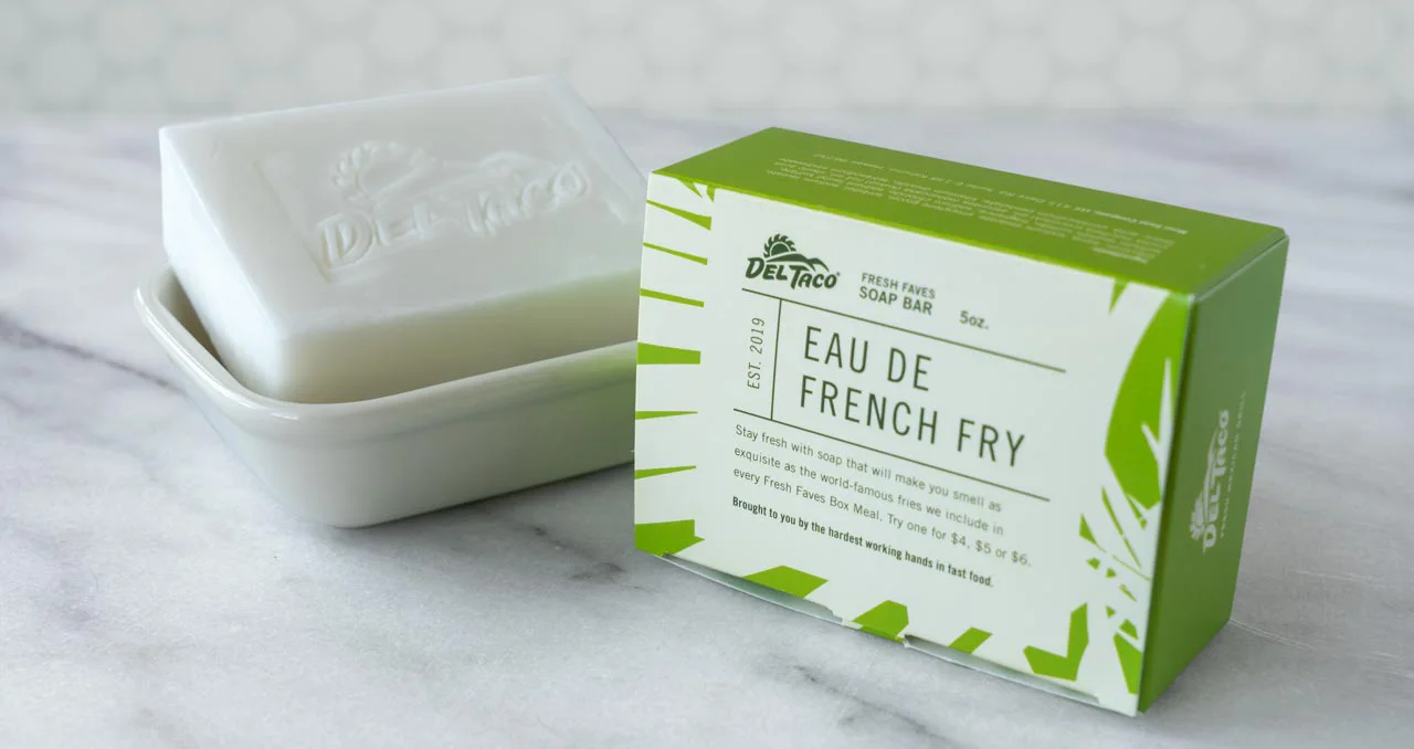 A bar of soap with the Del Taco logo sitting in a dish next to a box labeled "Eau de French Fry"