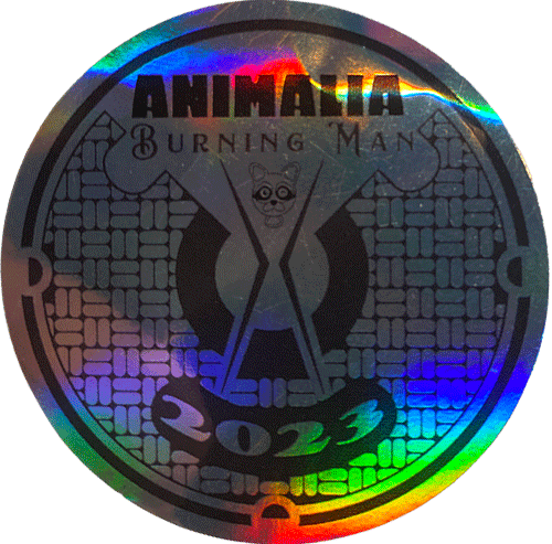 Holographic circular Burning Man sticker reading “Animalia 2023,” with the Man symbol and reflective rainbow foil surface.