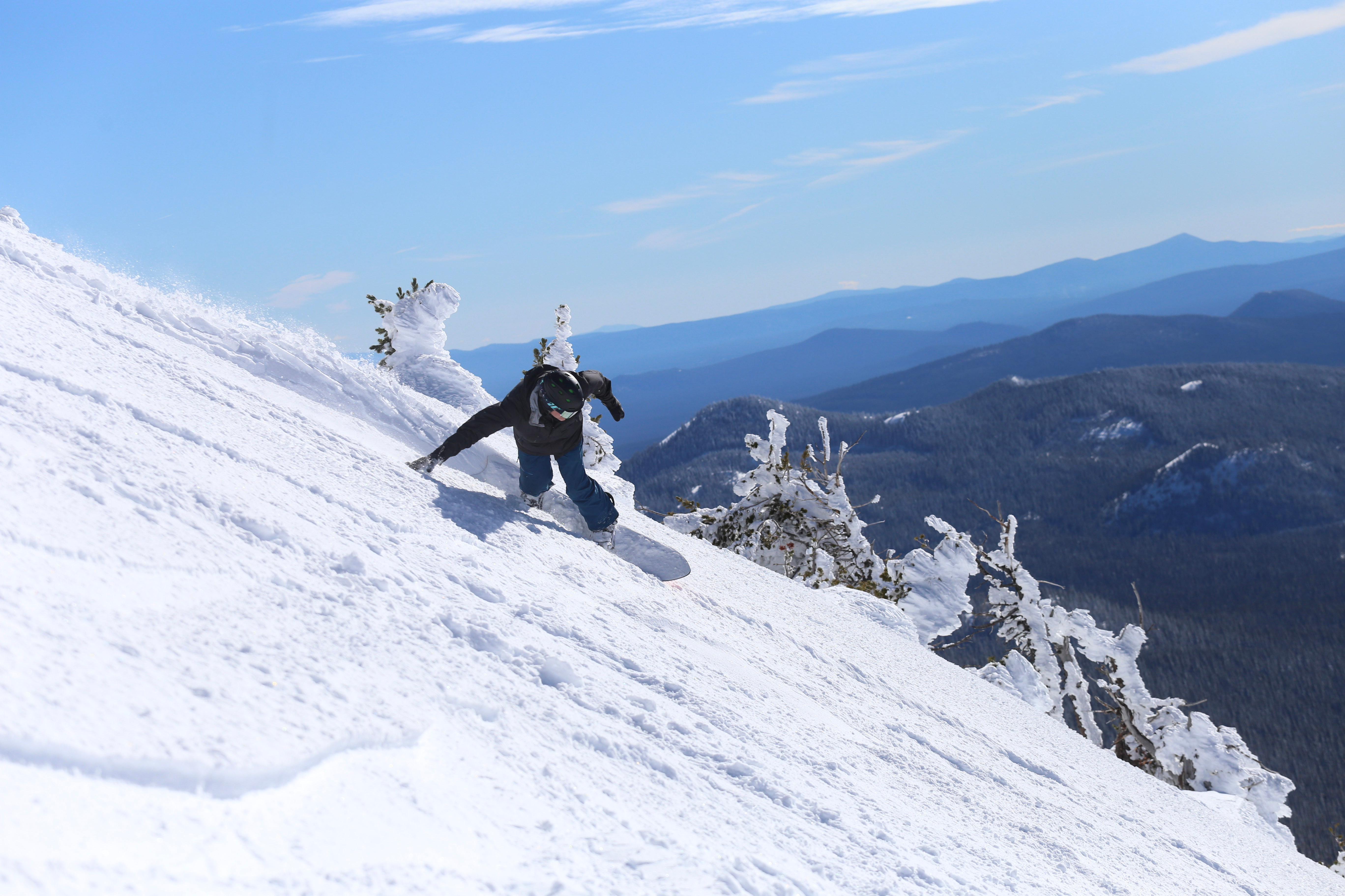 Shaun Vine snowboarding at Mt. Bachelor, on a steep slope with the valley in the background.