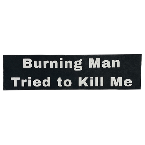 Black rectangular sticker with white text reading “Burning Man tried to kill me.”