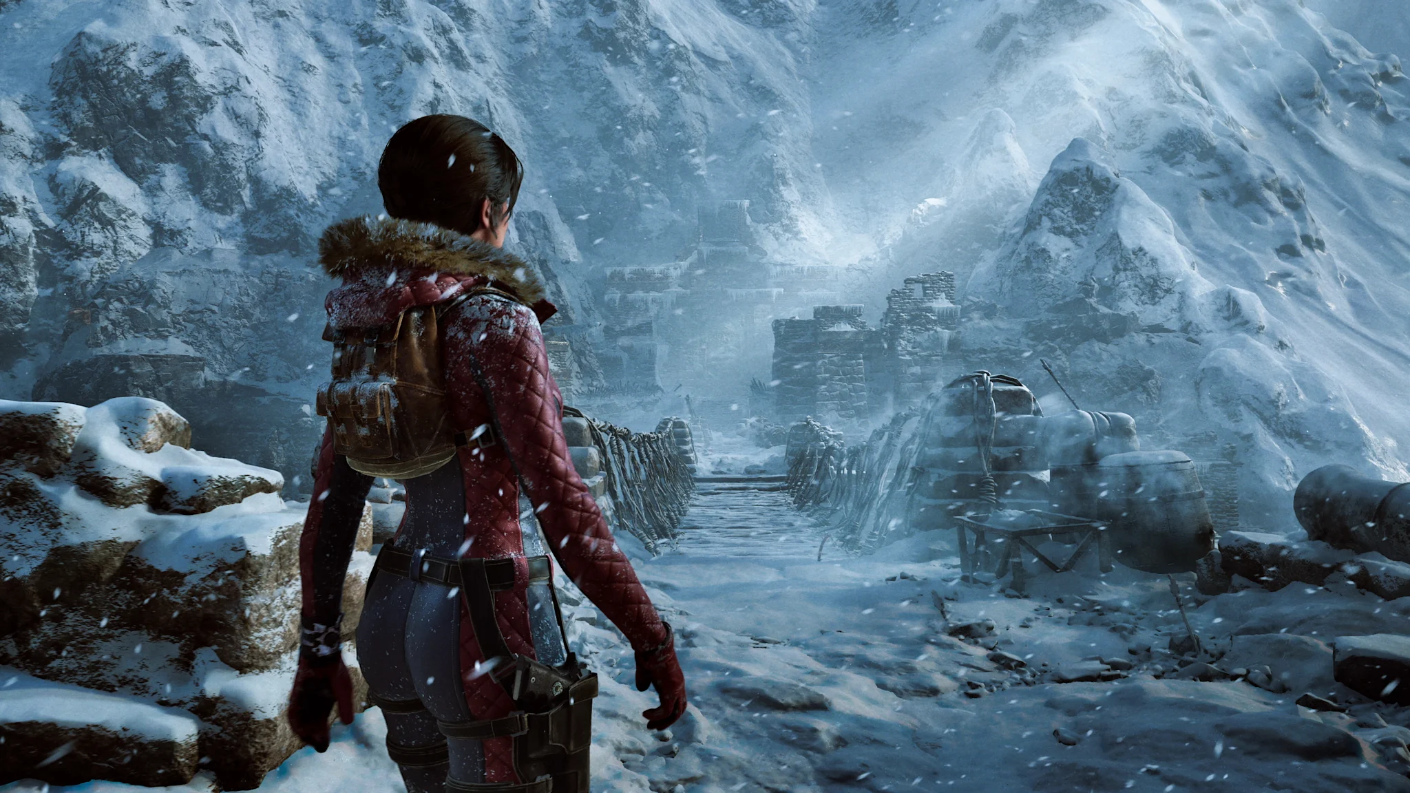 Female adventurer stands in a blizzard facing a wooden rope bridge leading to crumbling stone ruins nestled in an icy mountain canyon.