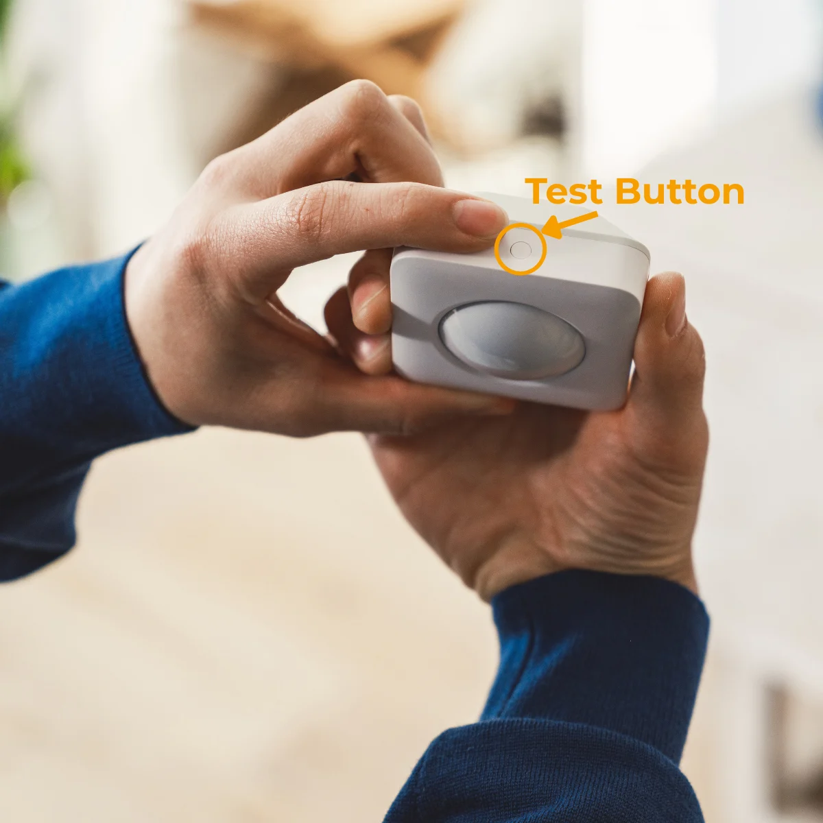 Someone holding the Motion Sensor Gen 2 in their hands with the Test Button facing up on the top of the device.