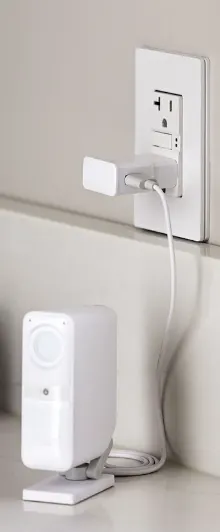 Smart Alarm Indoor Camera plugged into wall outlet on kitchen counter.