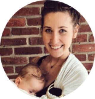 Woman smiling holding a baby posing in front of a brick wall