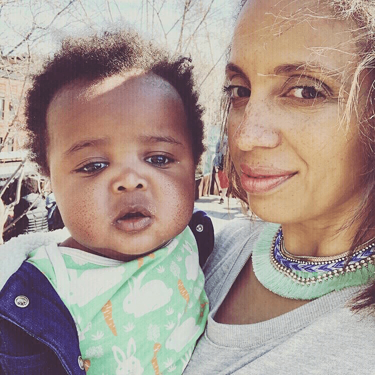 Woman holding a baby in a mint green shirt with white bunnies and orange carrots and a jean jacket