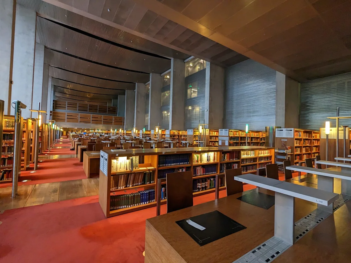 A long reading room with red carpet, wooden desks and rows of bookshelves