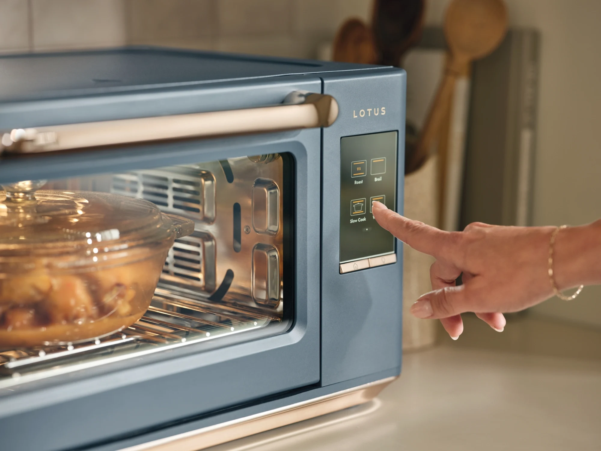 The Luminary oven in Bluestone with hand selecting Slow Cook mode on the touchscreen