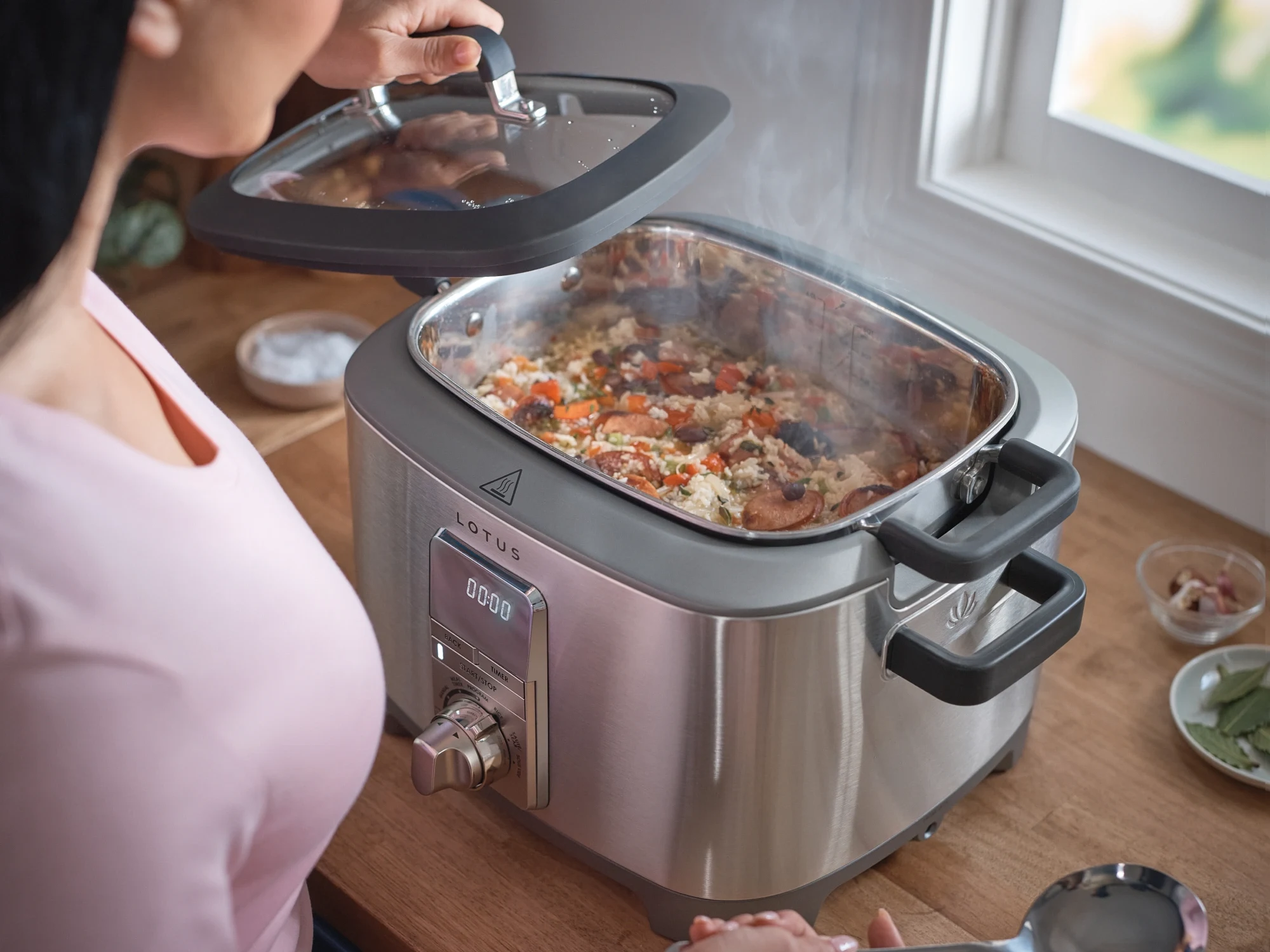 Lotus Professional Series The Sous multicooker with steam rising from a rice and sausage dish, lid being lifted