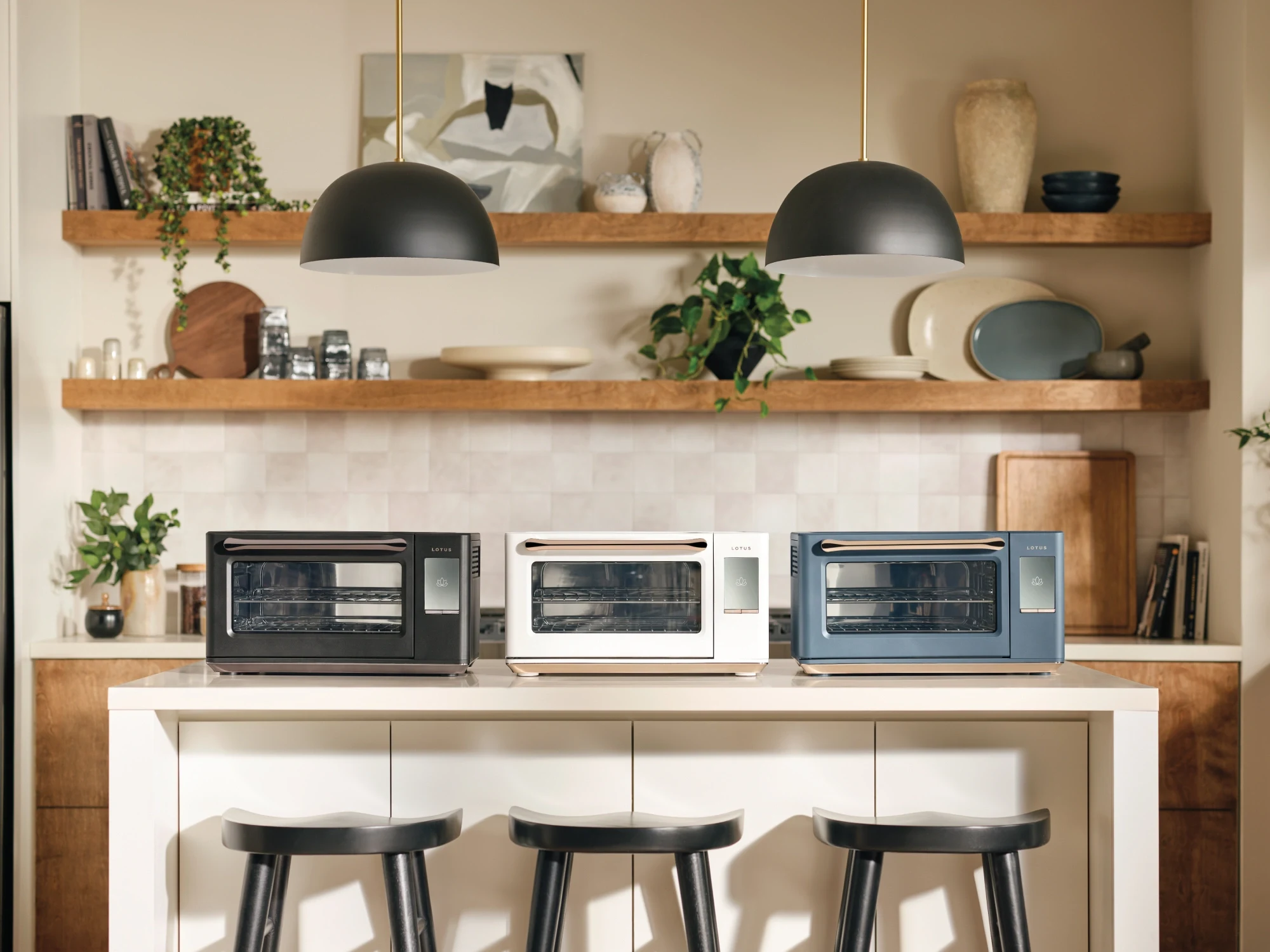 The Luminary oven shown in all three colorways, Obsidian, Alabaster, and Bluestone, lined up on a kitchen island