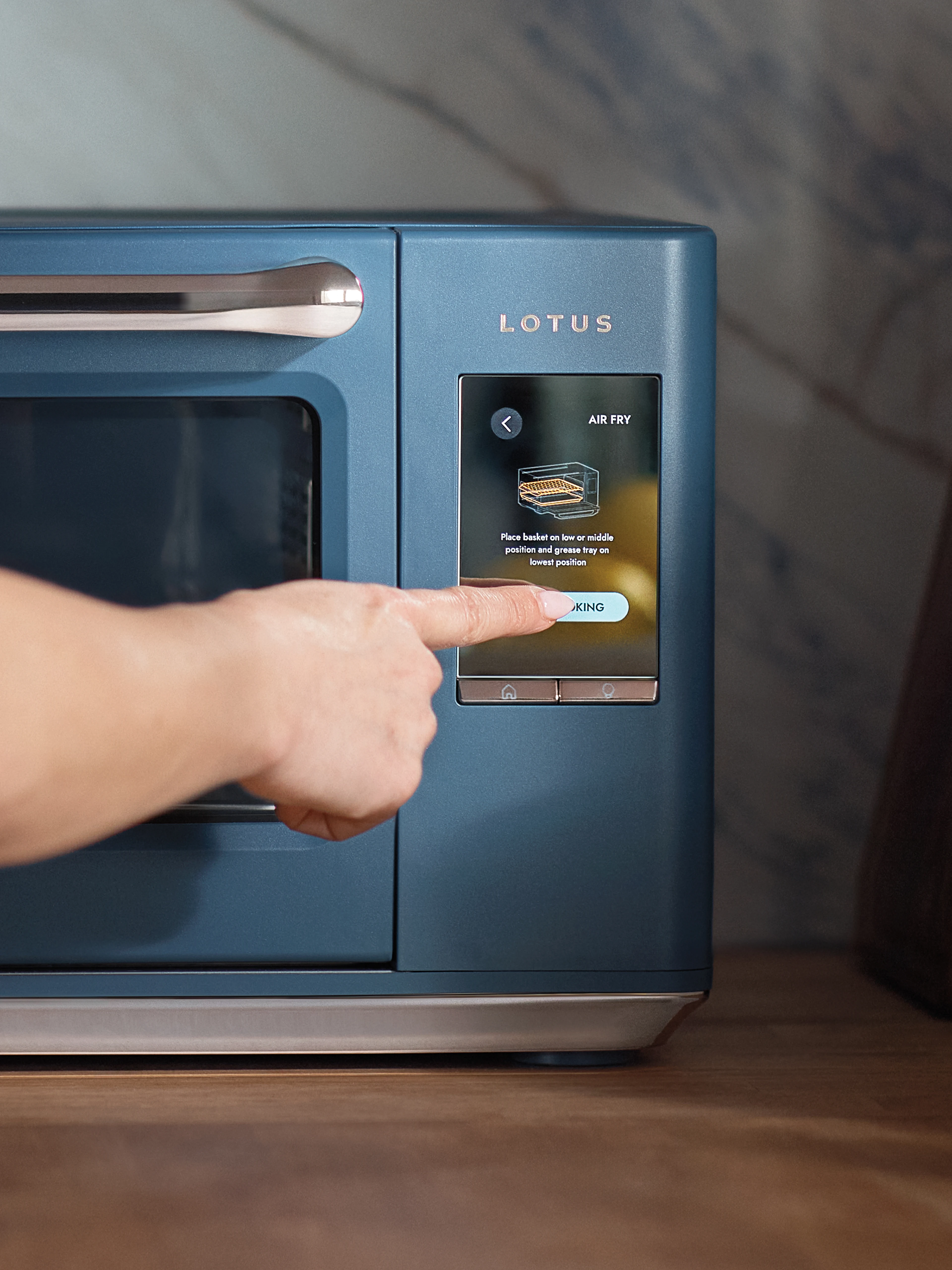 The Luminary oven in Bluestone with hand selecting Air Fry mode on the digital touchscreen