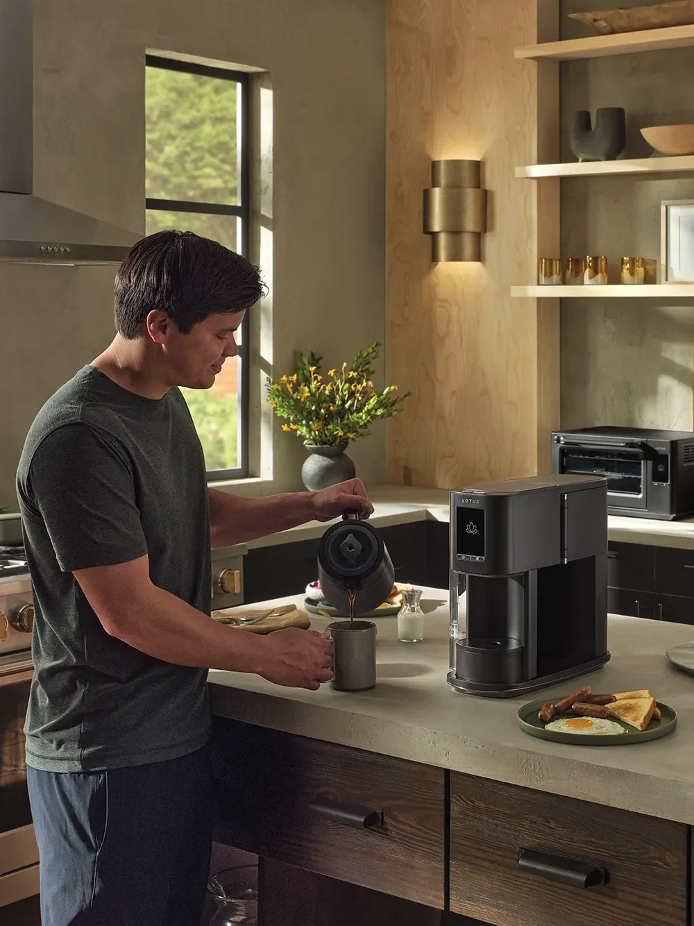 The Ritual coffee system in Obsidian on a kitchen island with a man pouring coffee from the insulated carafe into a cup