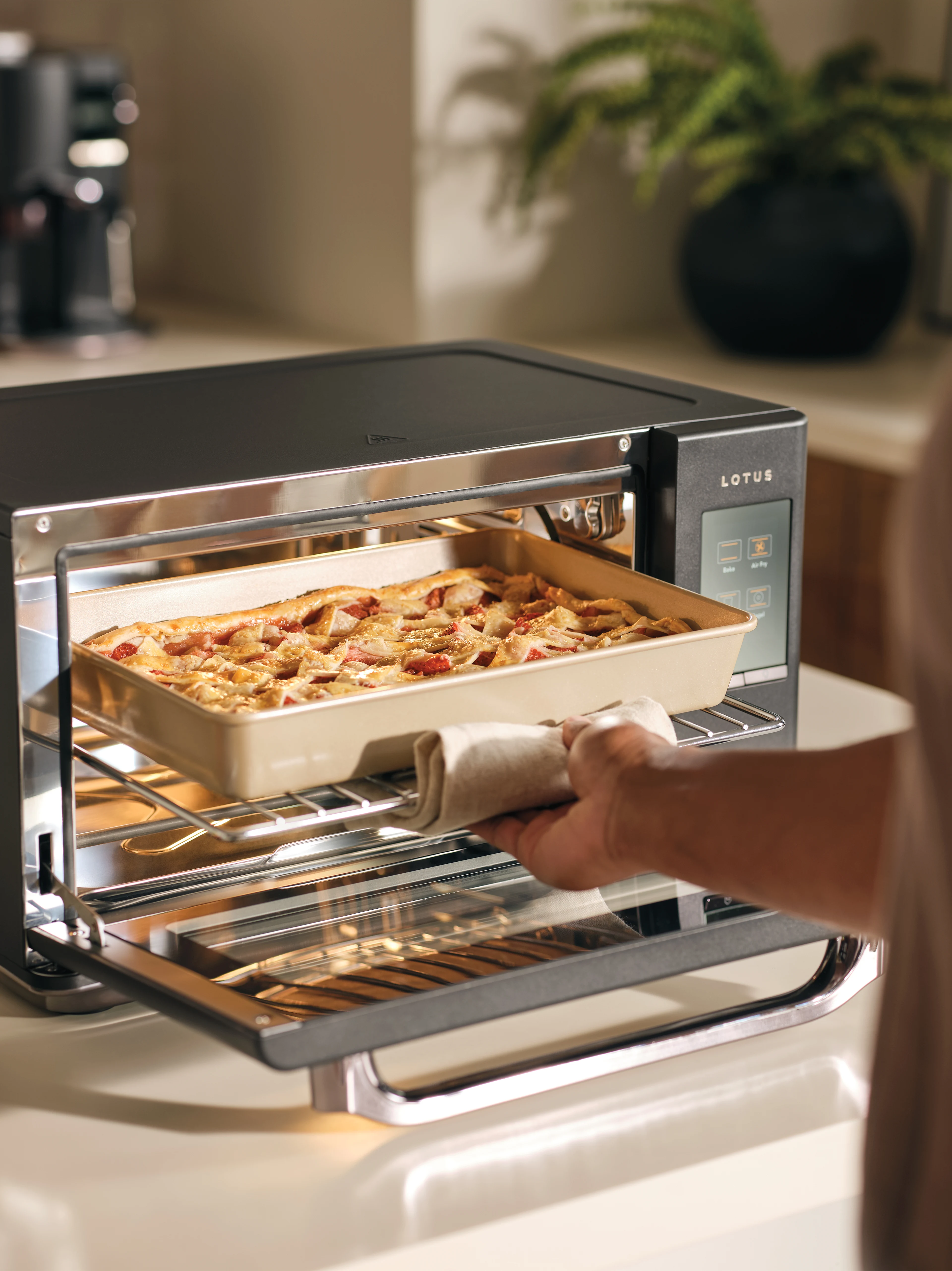 The Luminary oven in Obsidian with hand pulling out a warm tray of strawberry slab pie, using a folded cloth to protect from heat