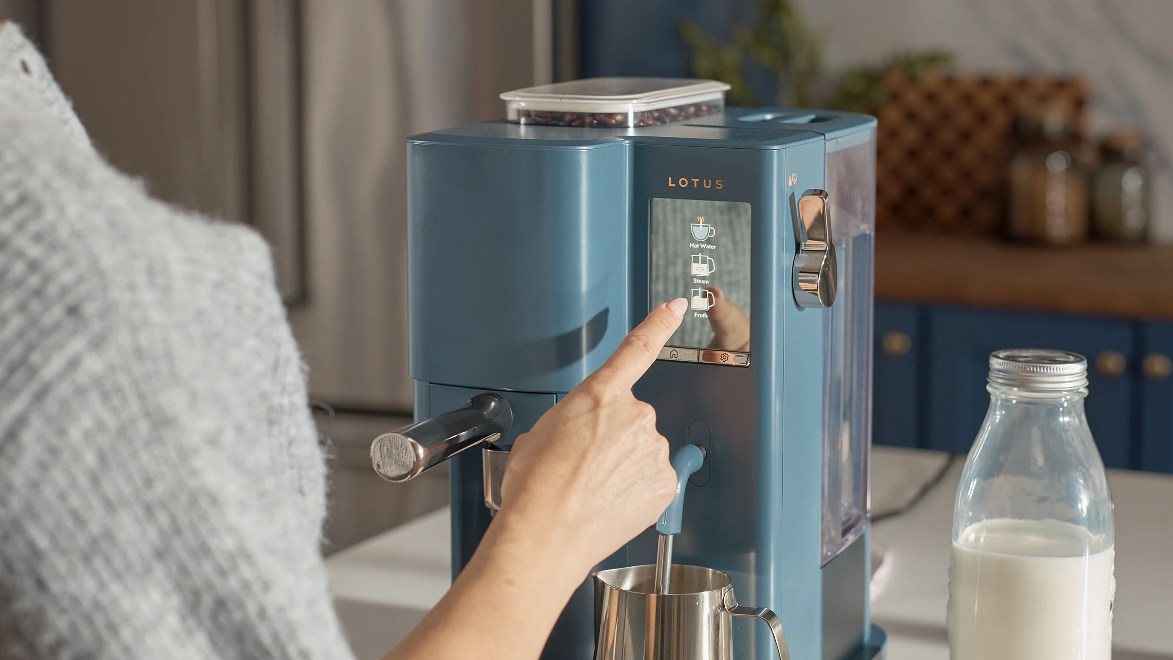 The Craft espresso machine in Bluestone with woman selecting a setting on the touchscreen while the steam wand froths milk