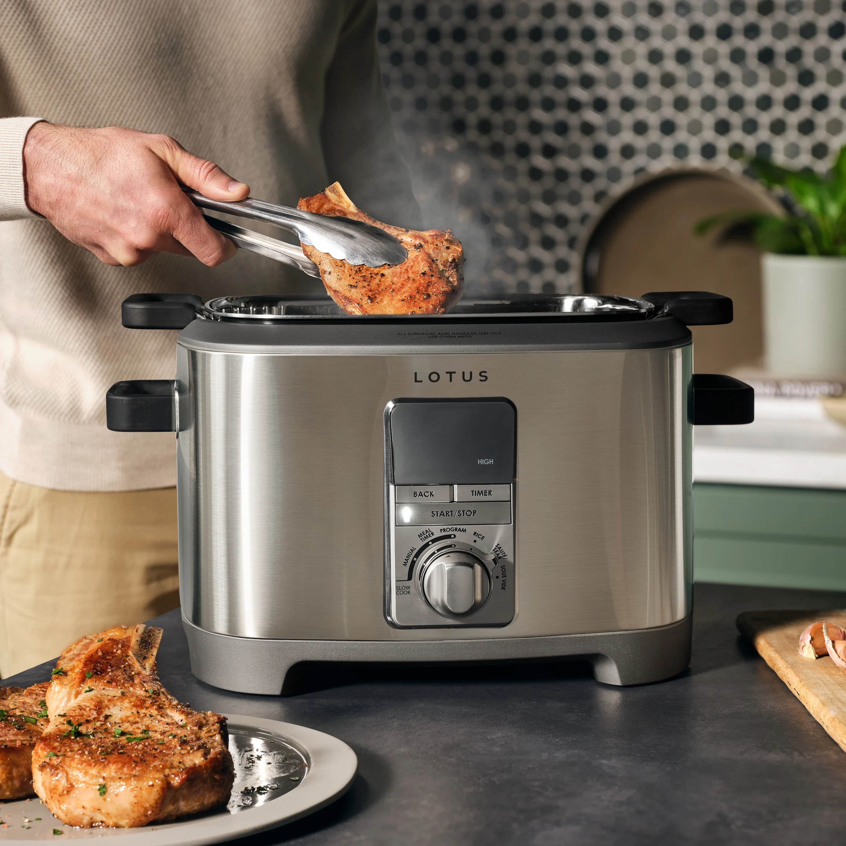 the sous™ multifunction cooker with digital touchscreen and stainless steel finish, shown in a modern kitchen with a man cooking pork chops inside versatile appliance for slow cooking steaming and pressure cooking