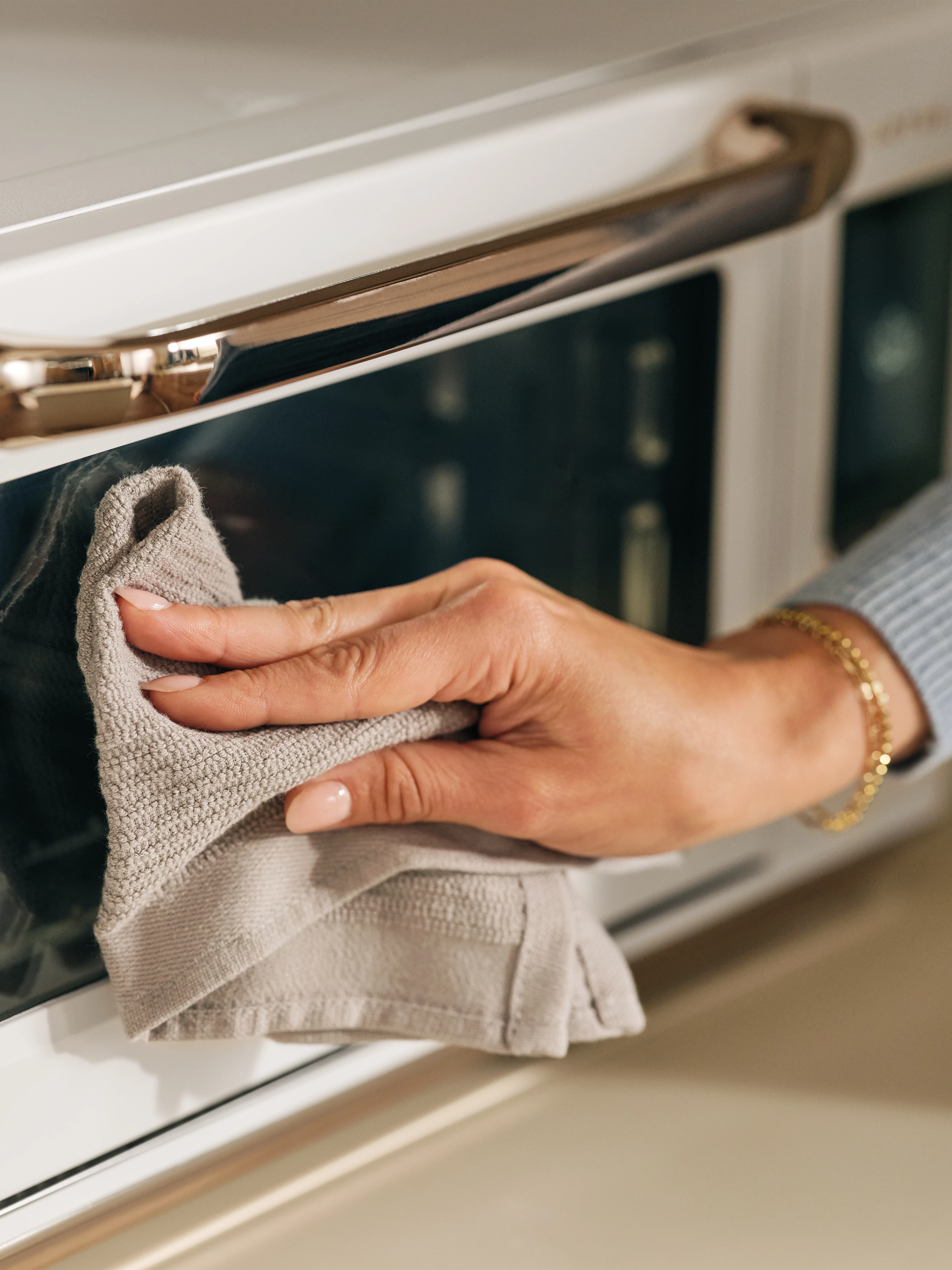 The Luminary oven in Alabaster with a hand wiping the exterior glass door clean using a cloth
