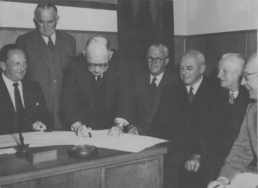 An image of Sir John Allum signing the Bridge contract with colleagues