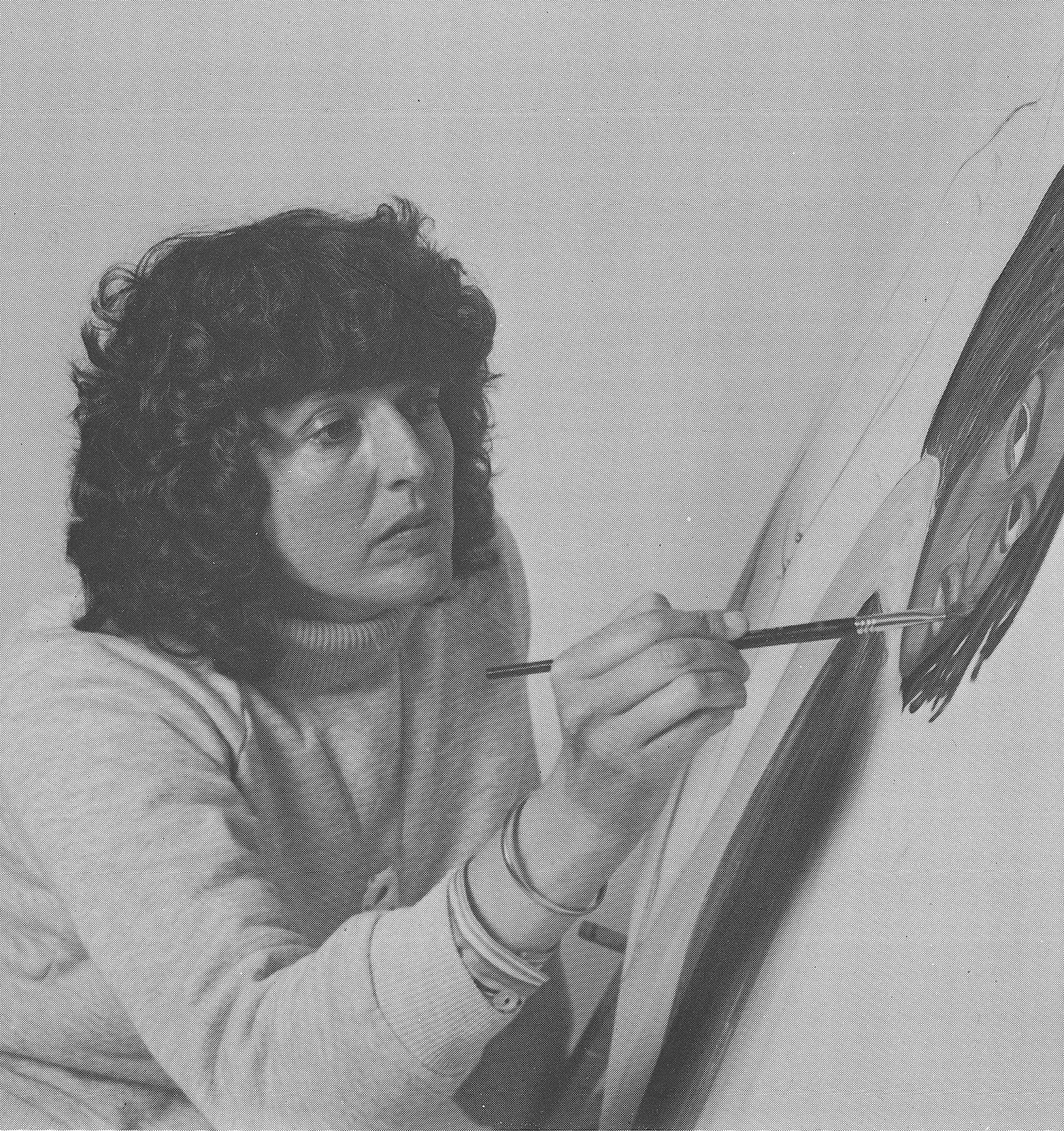 Black and white photo of a woman with curly hair painting a portrait with a brush.