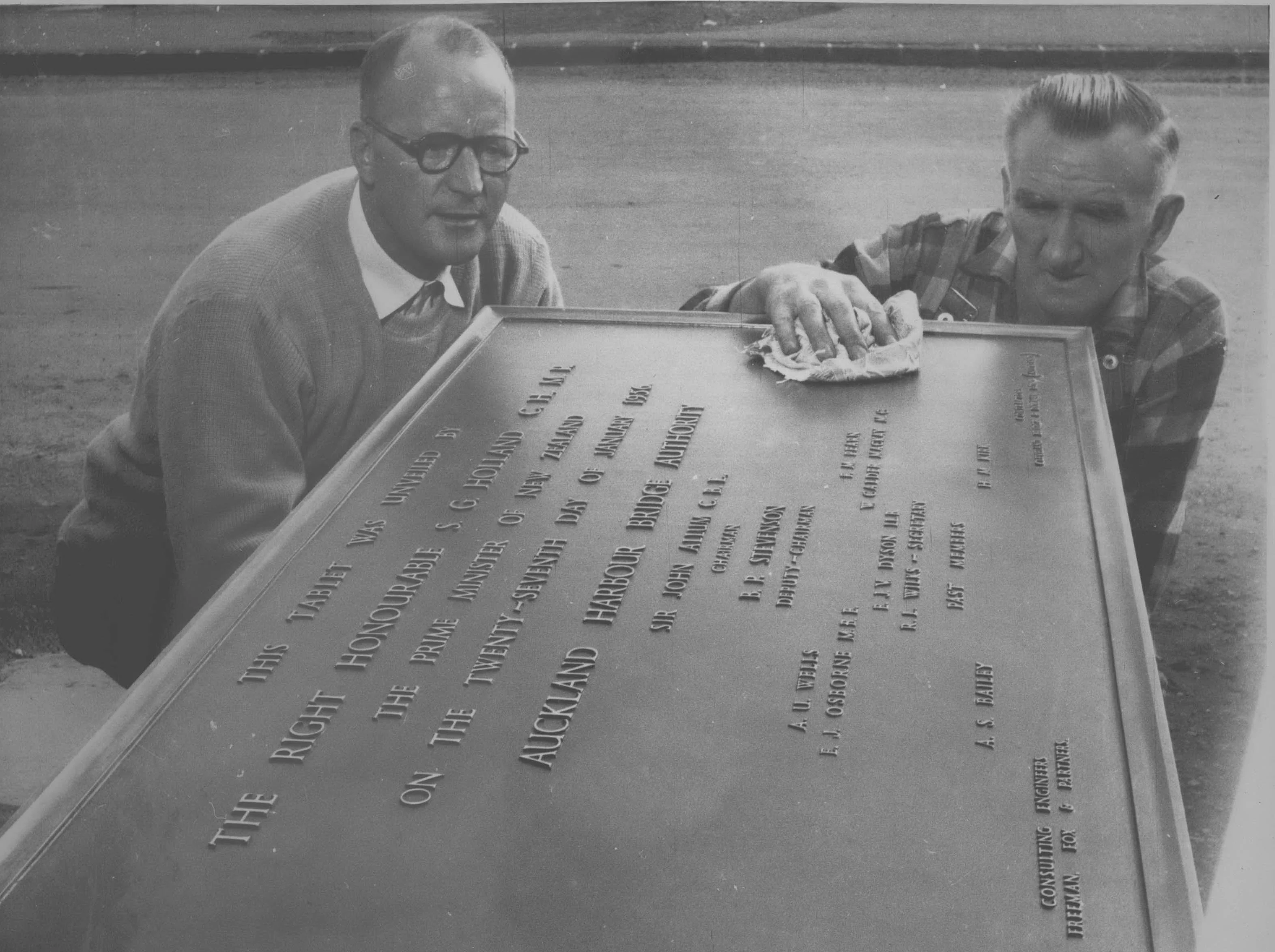 Two men polishing the plaque commemorating the foundation stone laying at the bridge.