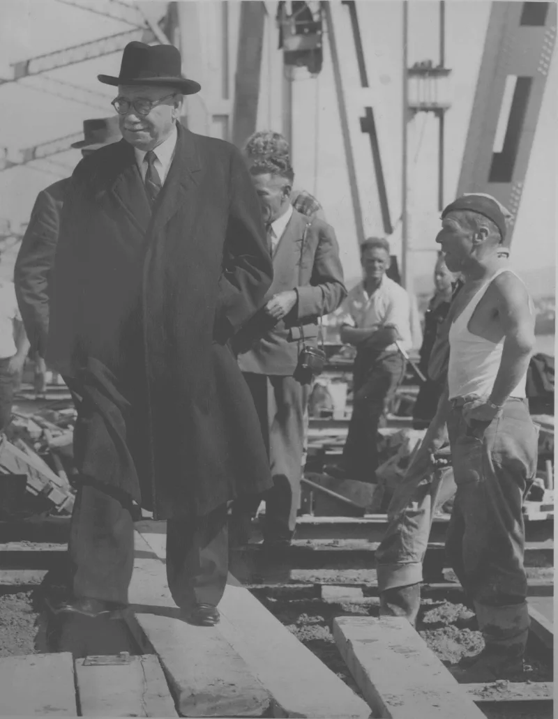 Sir John Allum crossing the complete Auckland Harbour Bridge with workers in the background