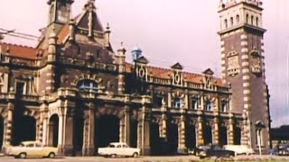 A brown and white heritage building with supporting pillars and high entrance, few cars parked in front