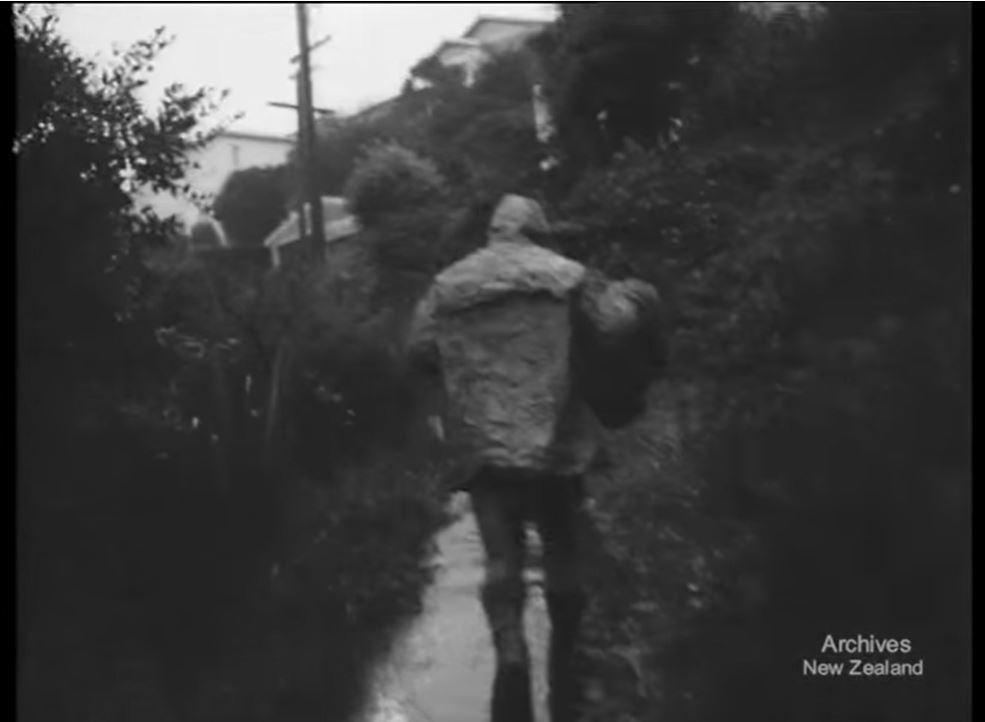 Still from the film 'Dustie'. A man walks up a narrow pathway carrying a bag of rubbish.
