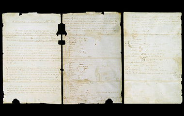 Three slightly torn and yellowed papers with writing in dark brown on a black background 