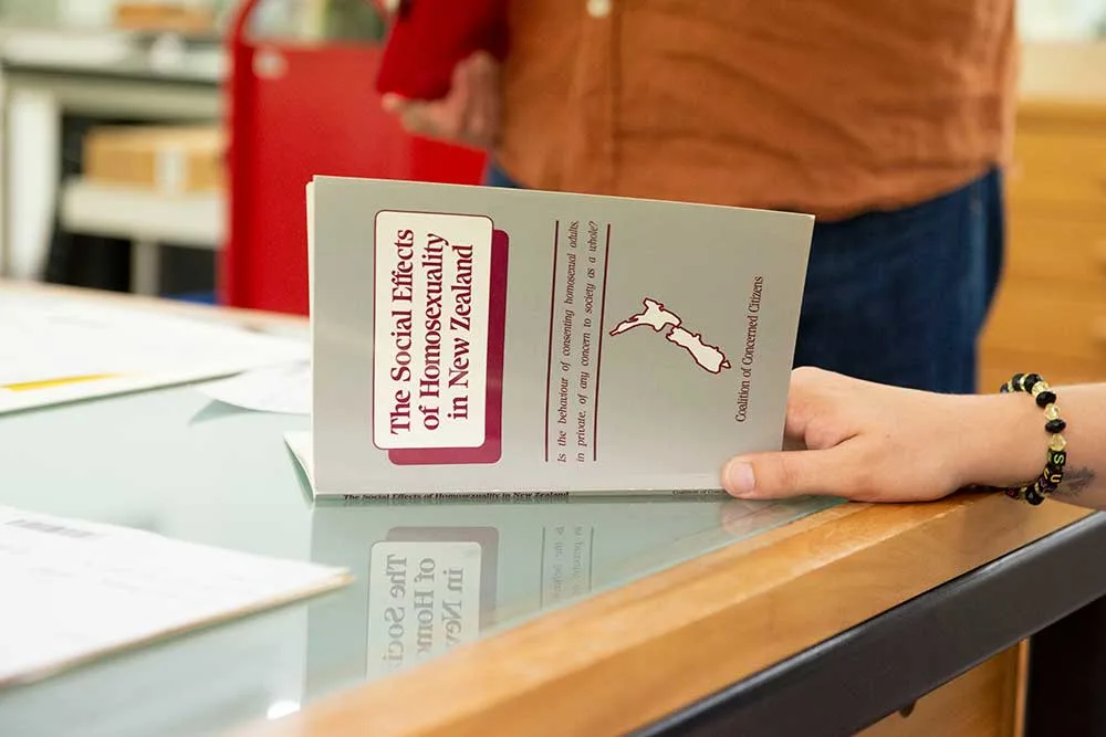 Close up of a hand opening a book "The social effects of Homosexuality in New Zealand, Coalition of Concerned Citizens"