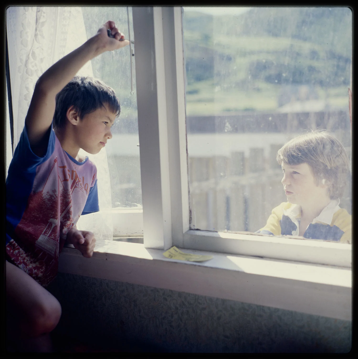 A young boy looking out of a glass window, a boy standing outside and looking at him  