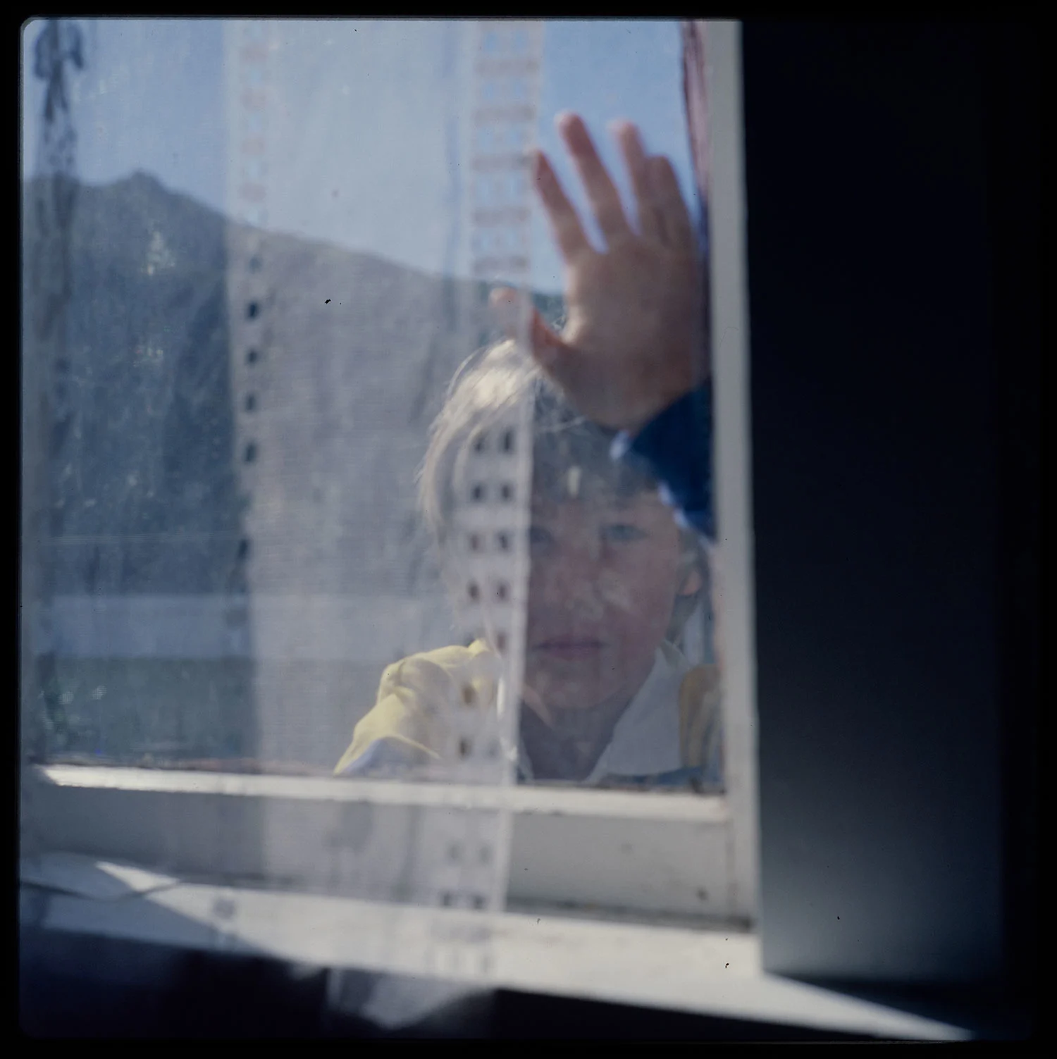 A boy standing outside a glass window with his left hand touching the glass