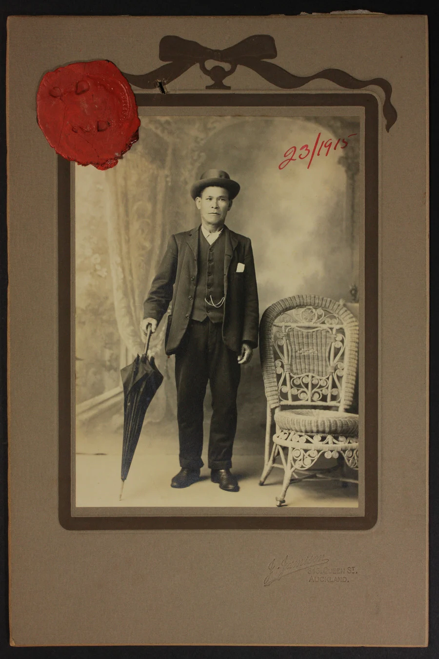 Hong Yuen stands posing for a portrait in a photography studio. He’s wearing a 3-piece suit and hat, and is holding an umbrella.