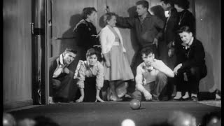 A still from 'Pictorial Parade No. 79'. A group of teens play bowls. Crouched on the floor, they watch the ball intently as it rolls.