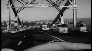 Black and white photo of a road with cars and a metal overbridge
