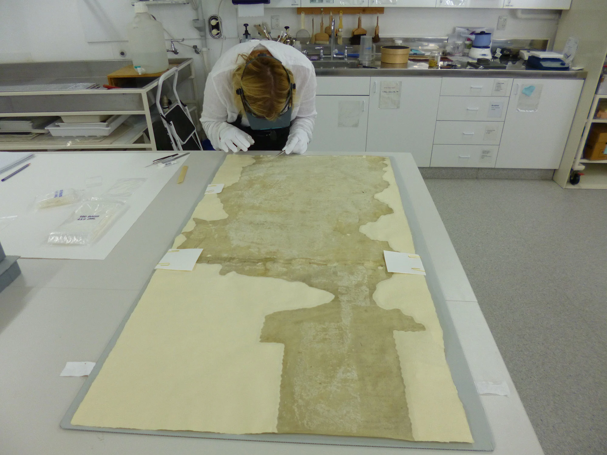 A conservator bending down on a table that has an old sheet