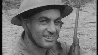 A black and white close up photo of a smiling man wearing a hard hat and holding a gun