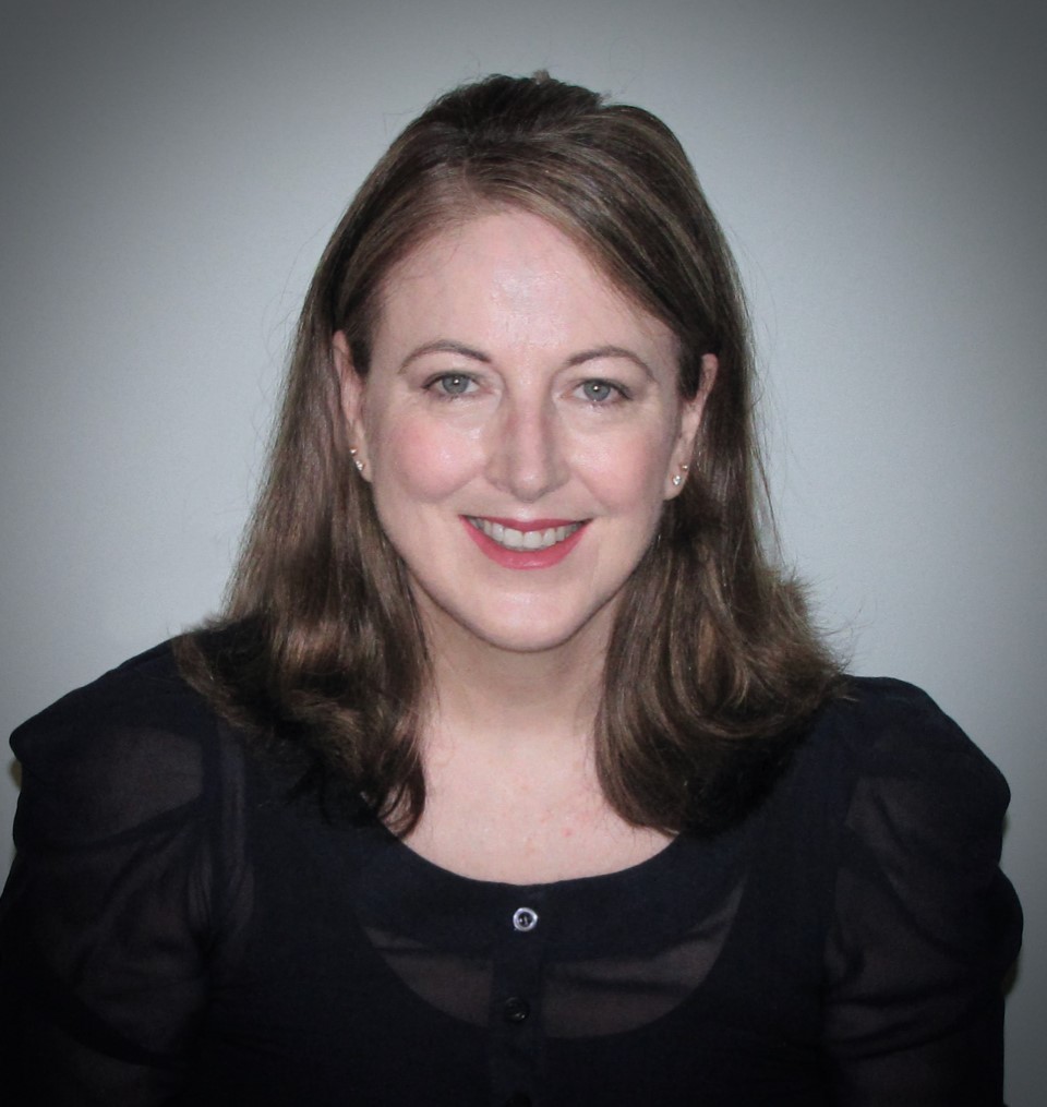 A closeup photo of smiling woman with shoulder length brown hair and wearing a black dress. 