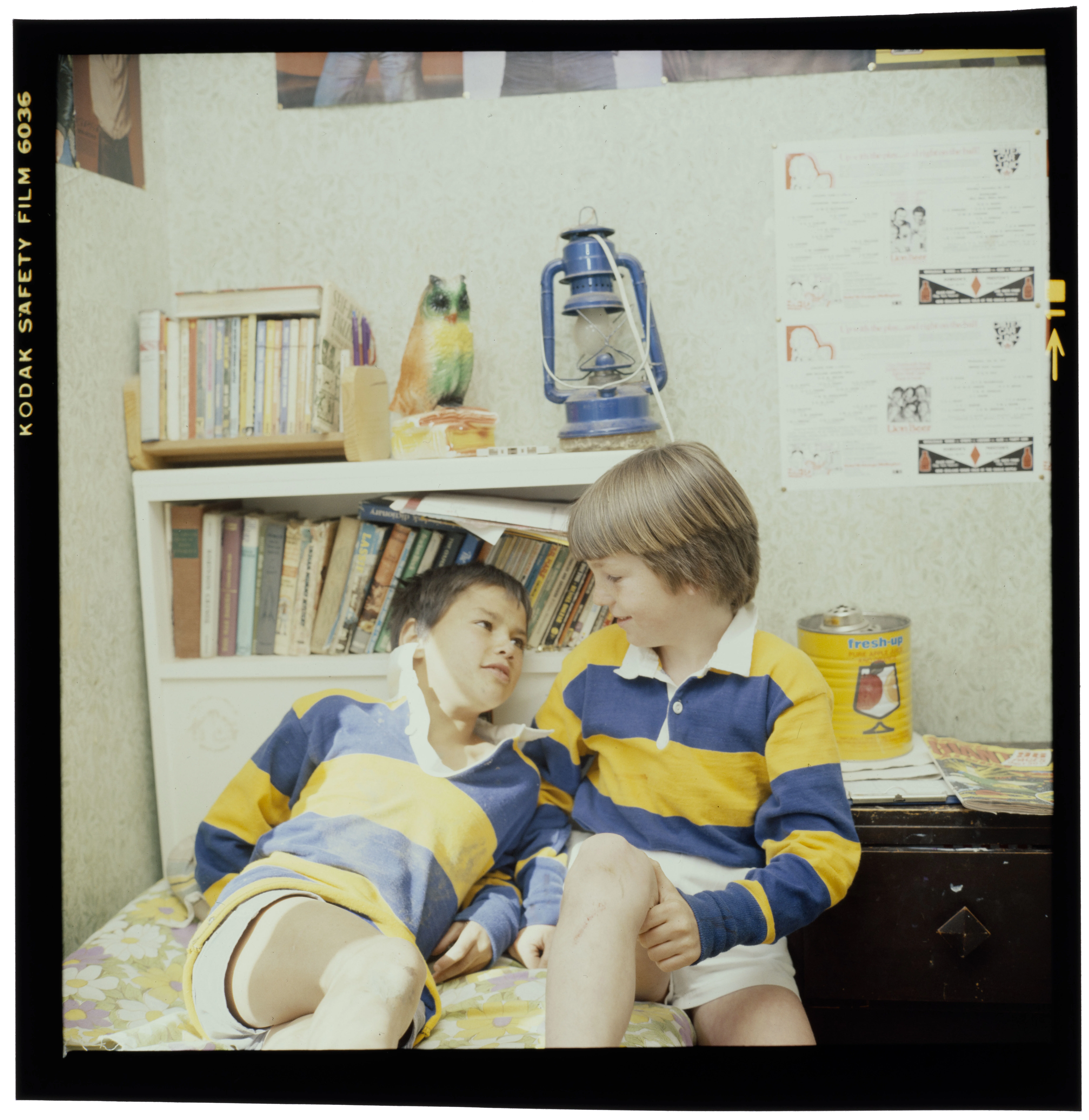Two boys wearing blue and yellow striped shirts sitting on a bed smiling at each other