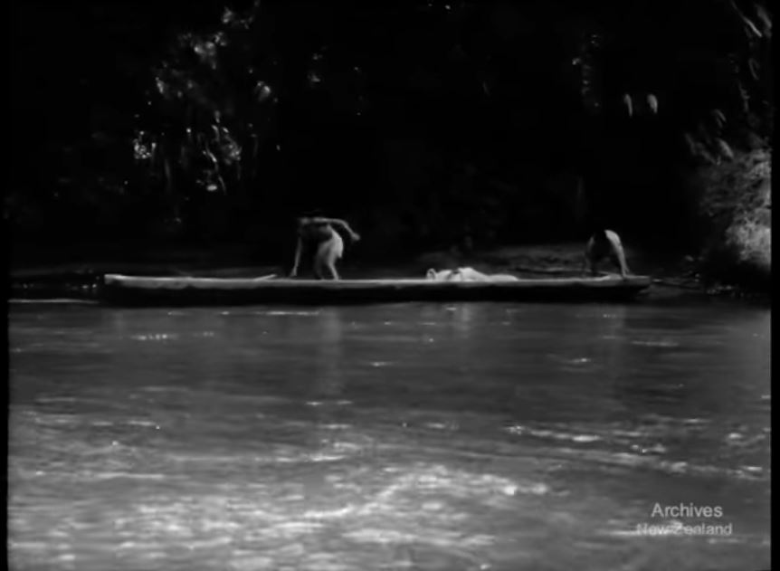 A still from 'The legend of the Wanganui River'. Two people push a canoe out from a river bank.