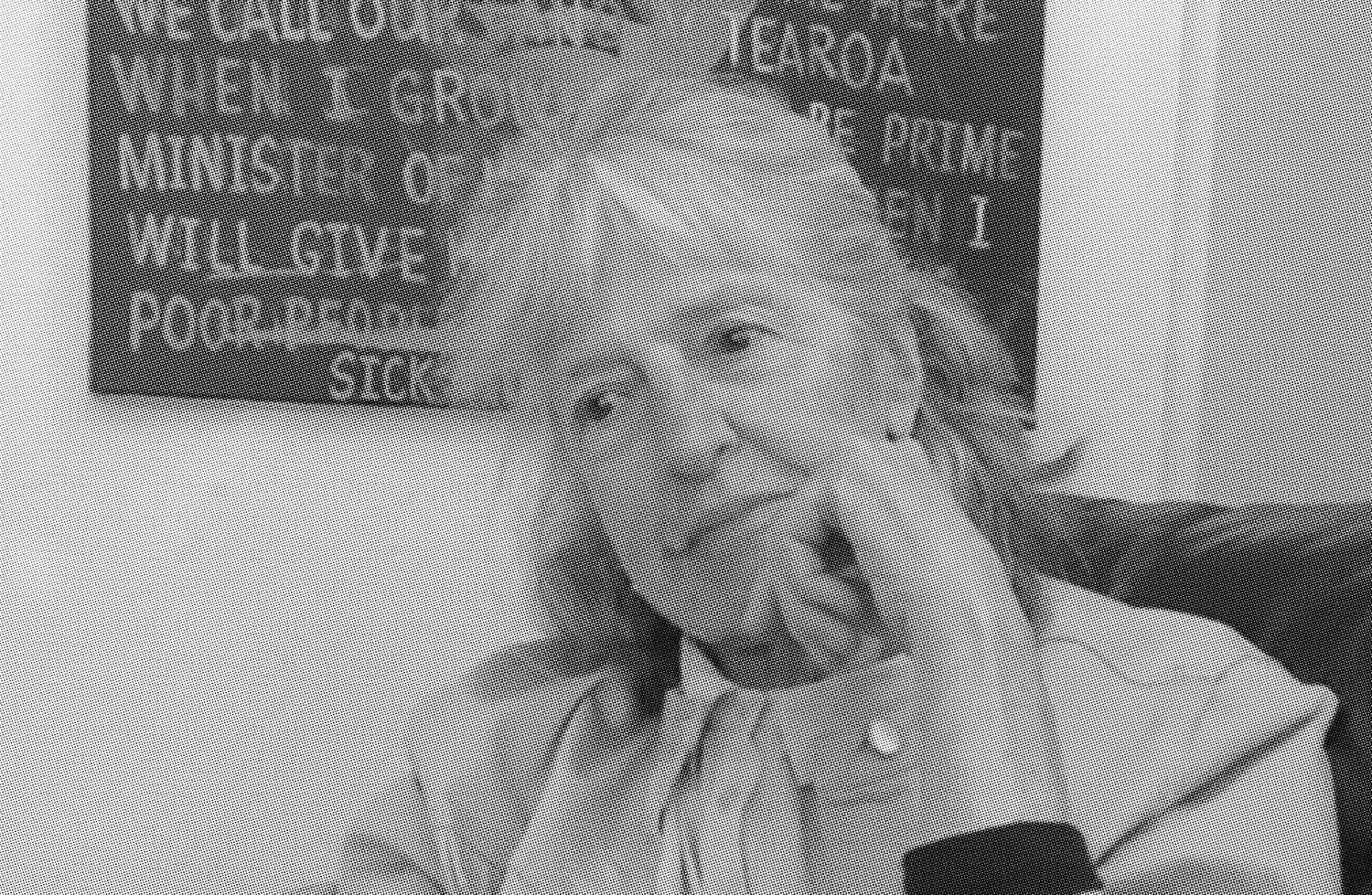 Black and white photo of an old woman sitting with her left hand near her face, a poster hangs behind her on the wall.