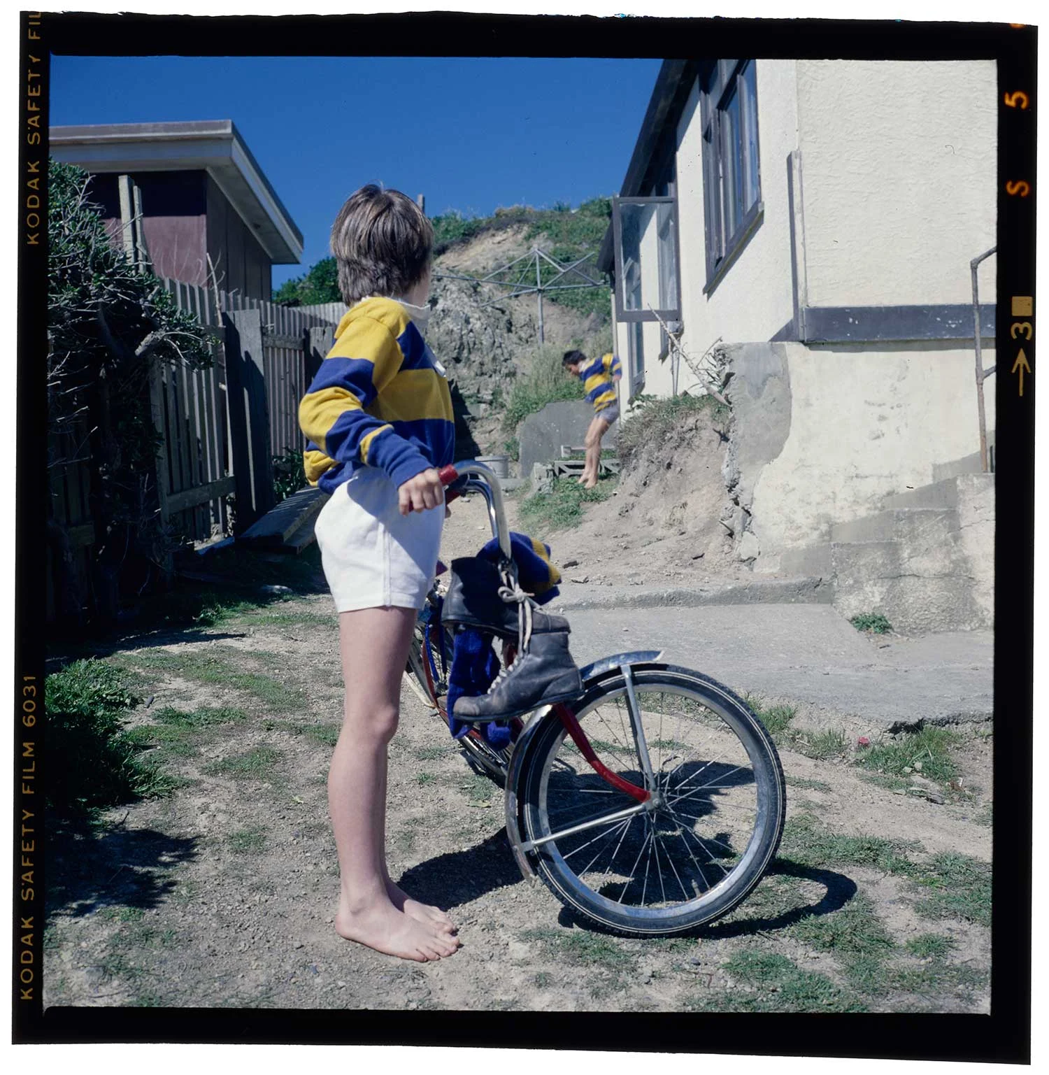 A boy wearing a blue and yellow striped shirt holding a bike, standing outside a house