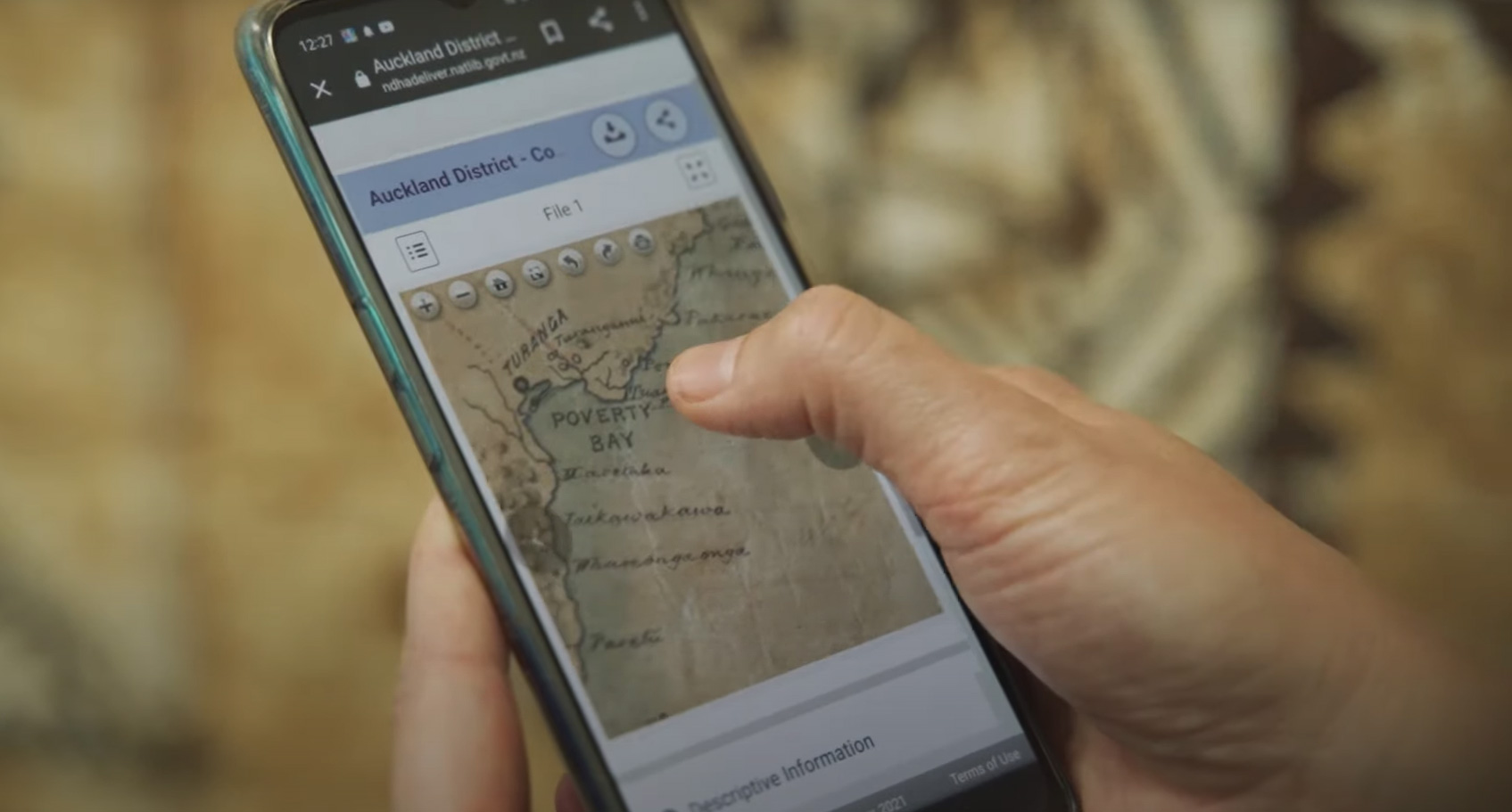 A hand holding a phone with a map on a brown blurred background  