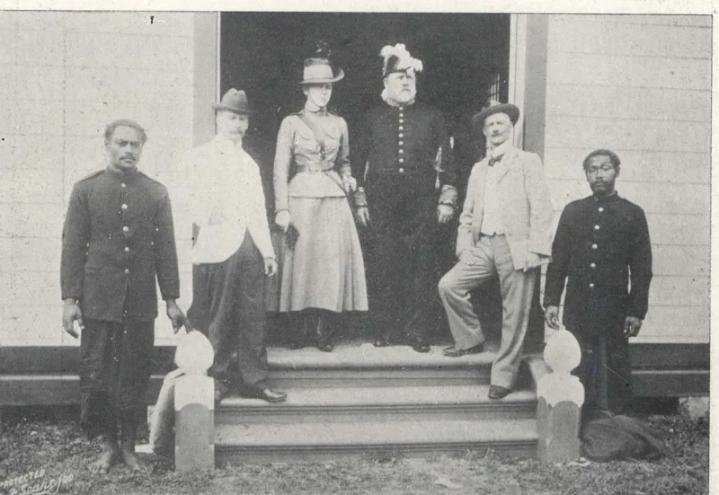 Black and white photo of a group of people standing on an entrance to a house