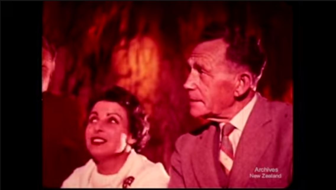 A still from the film 'Valley of Waitomo' showing two people inside the Waitomo Caves, illuminated in red light.