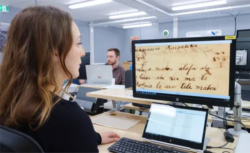 Archivist Wikitoria Rakete checks the quality of a recently-digitised item sitting in front of a computer sceen with a close up displayed on-screen