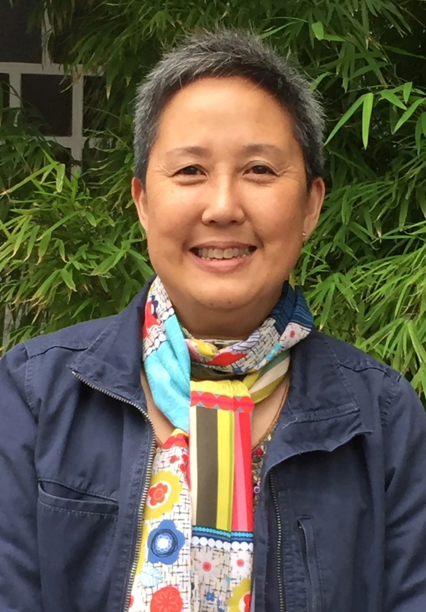 Close up of a smiling woman wearing blue shirt and colorful scarf around her neck and short hair