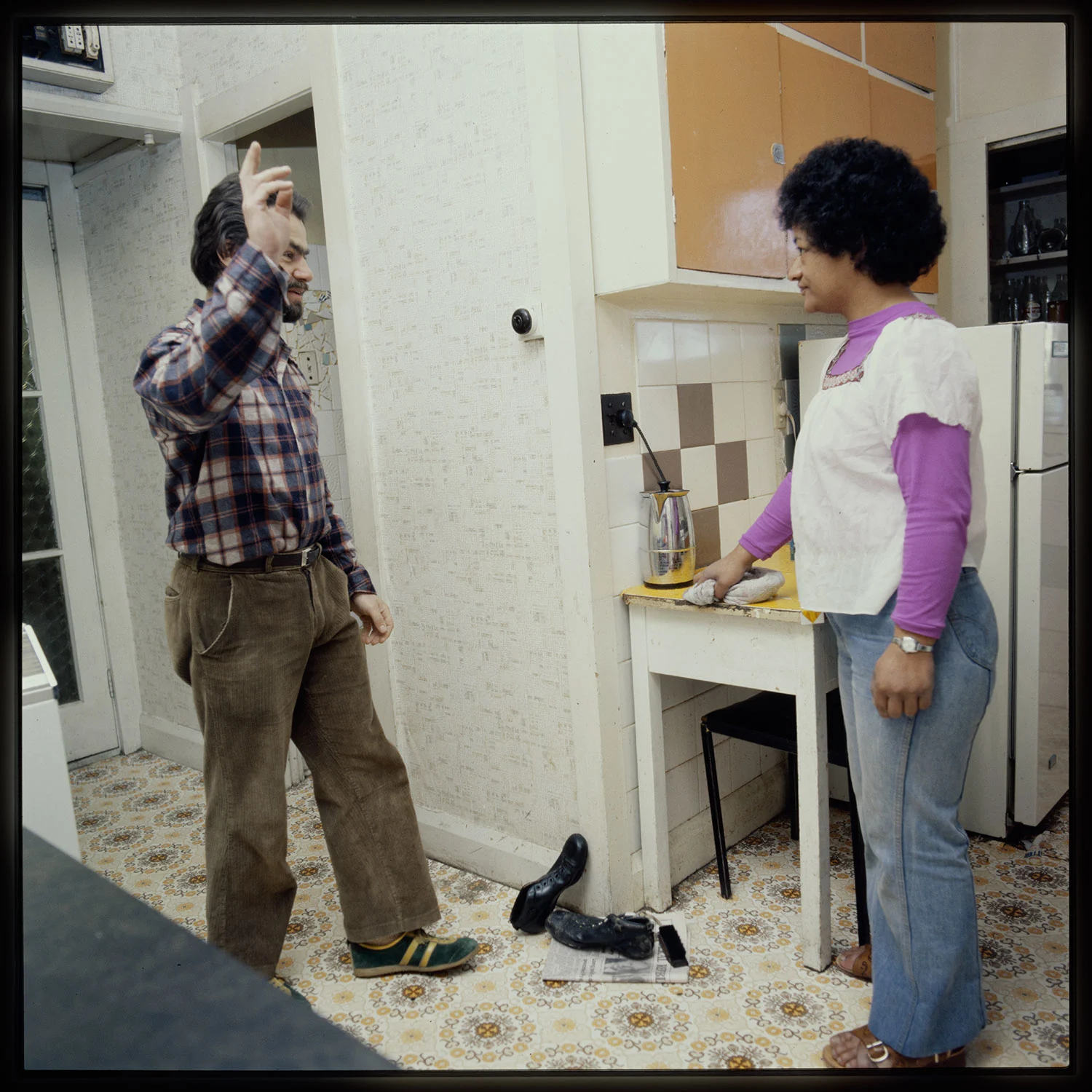 A woman with shorthair wearing a purple long sleeves shirt and white top standing in a kitchen, a bearded man standing in front of her