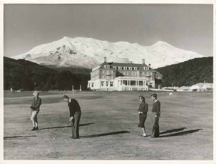4 Golfers on a golf course with a chateau and snow clad mountain in the background