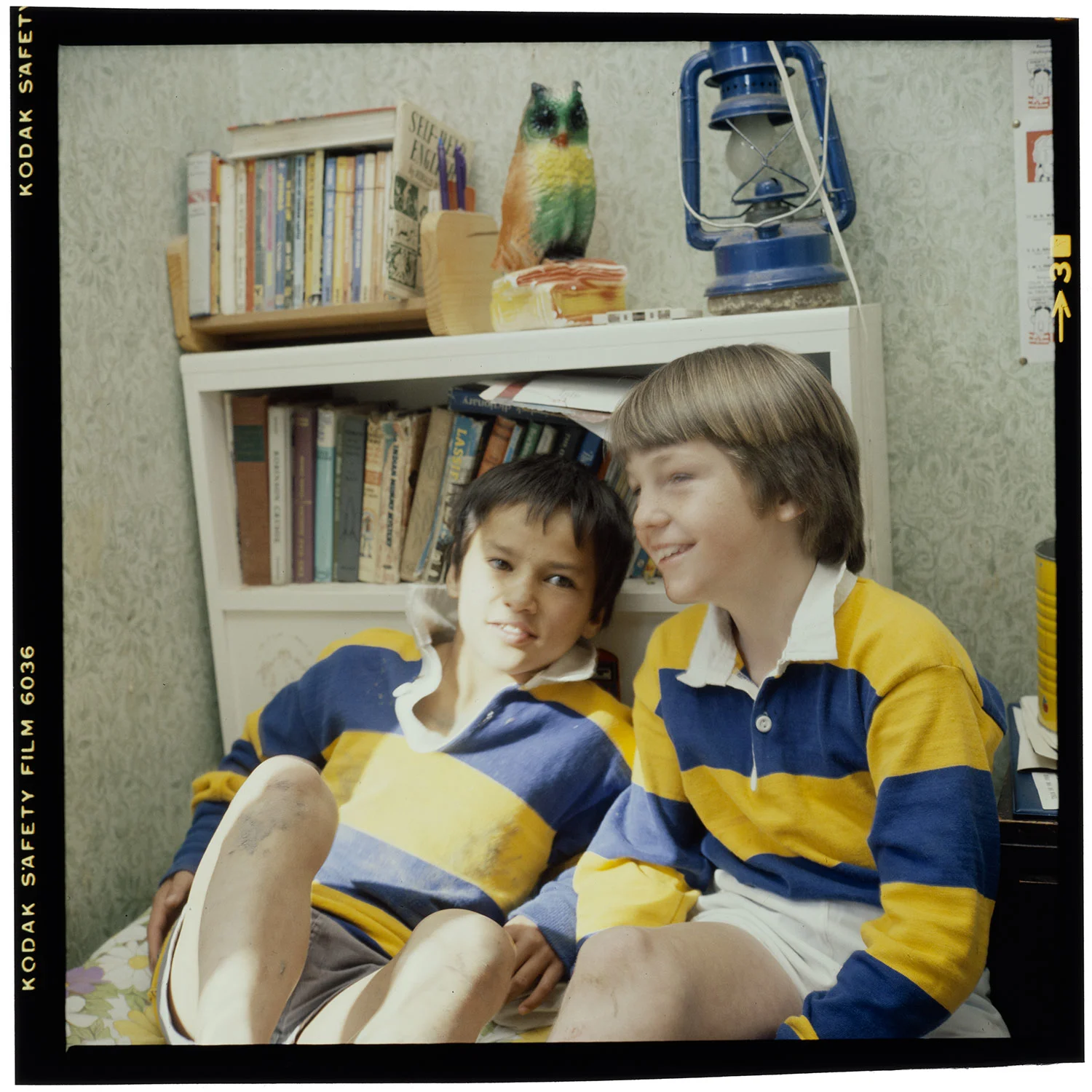 Two young boys wearing blue and yellow stripes shirts sitting on a bed