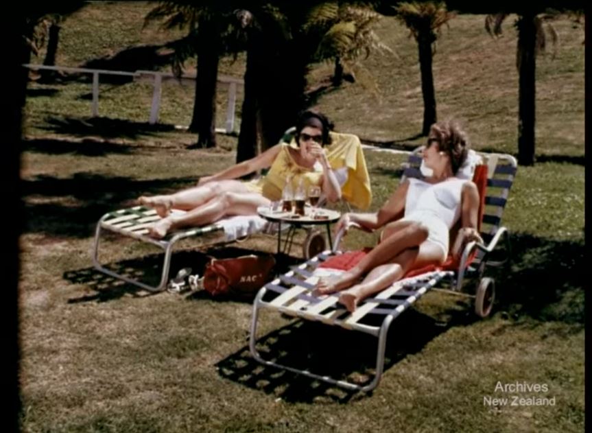 A still from 'Holiday for Susan'. Two women recline on lounge chairs in the sunshine.