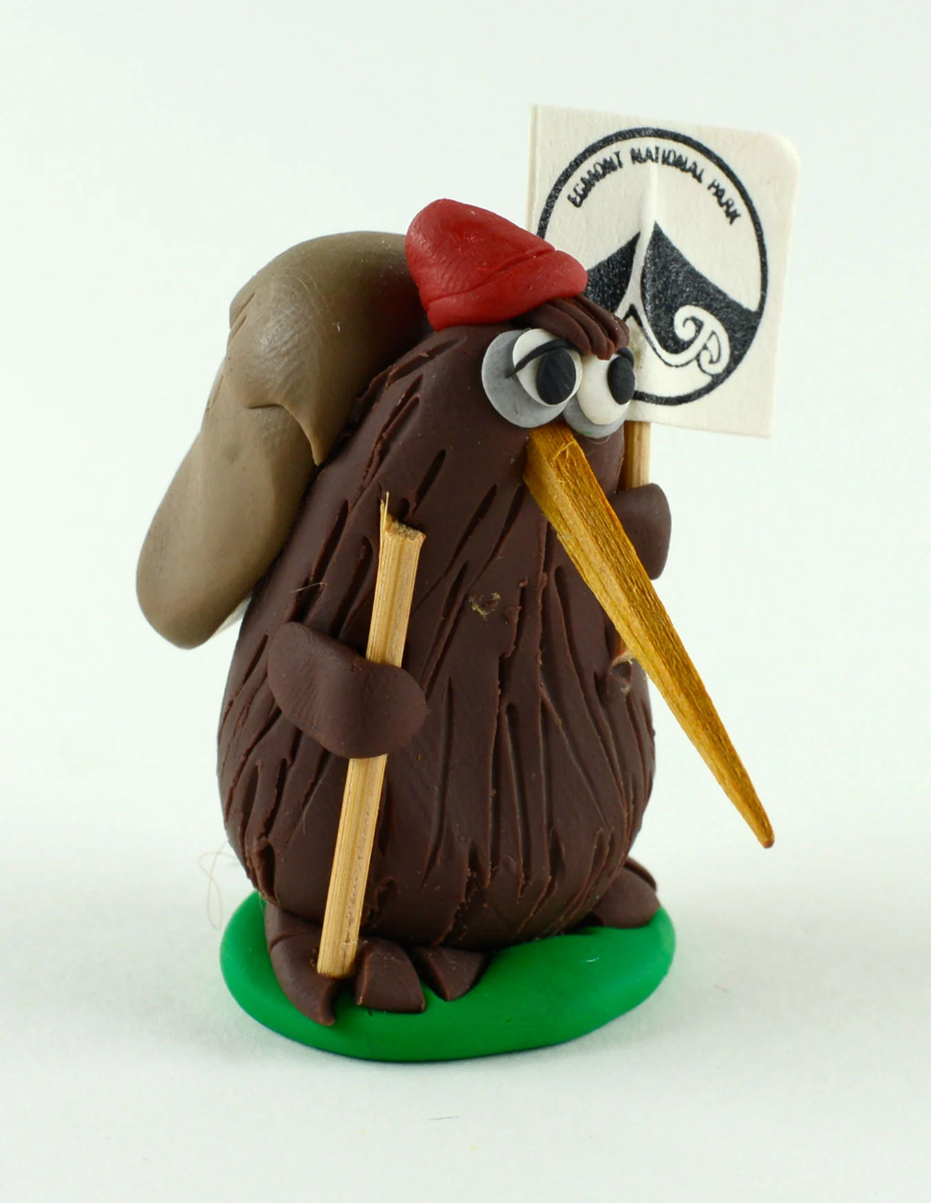 A brown figurine with a red hat, a long yellow beak and a back pack holding a yellow stick