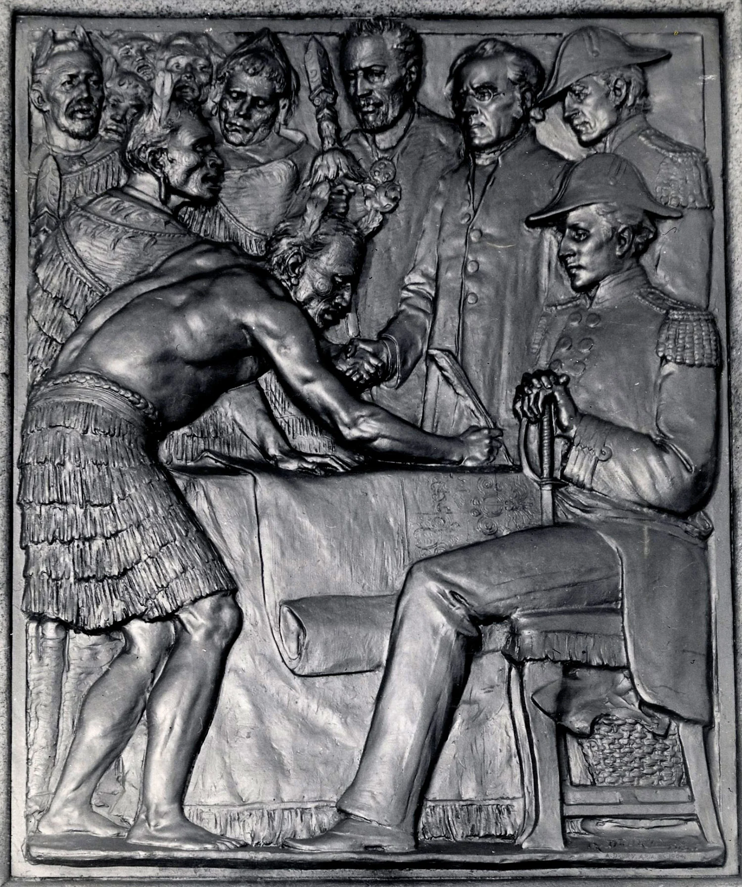 An embossed black plaque showing a man bending over a table, a man sitting on a chair while a group of people watch him